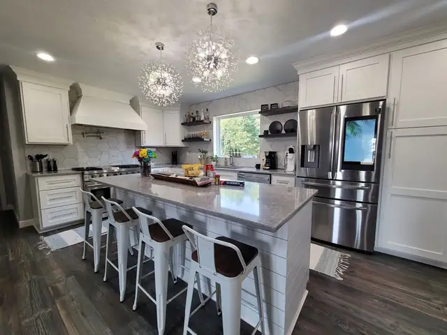 White kitchen with gray granite island, bar stools, crystal pendant lights and stainless French door refrigerator
