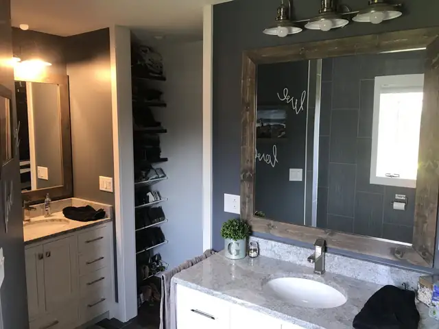 Bathroom with white vanity cabinets, gray granite top, rustic wood-framed mirror and tall built-in shelving
