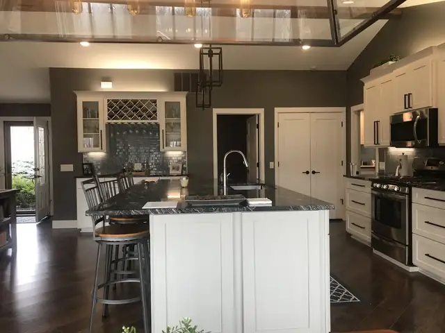 Kitchen island with dark granite countertop and white cabinets, bar stools and glass-front upper cabinets with a wine rack